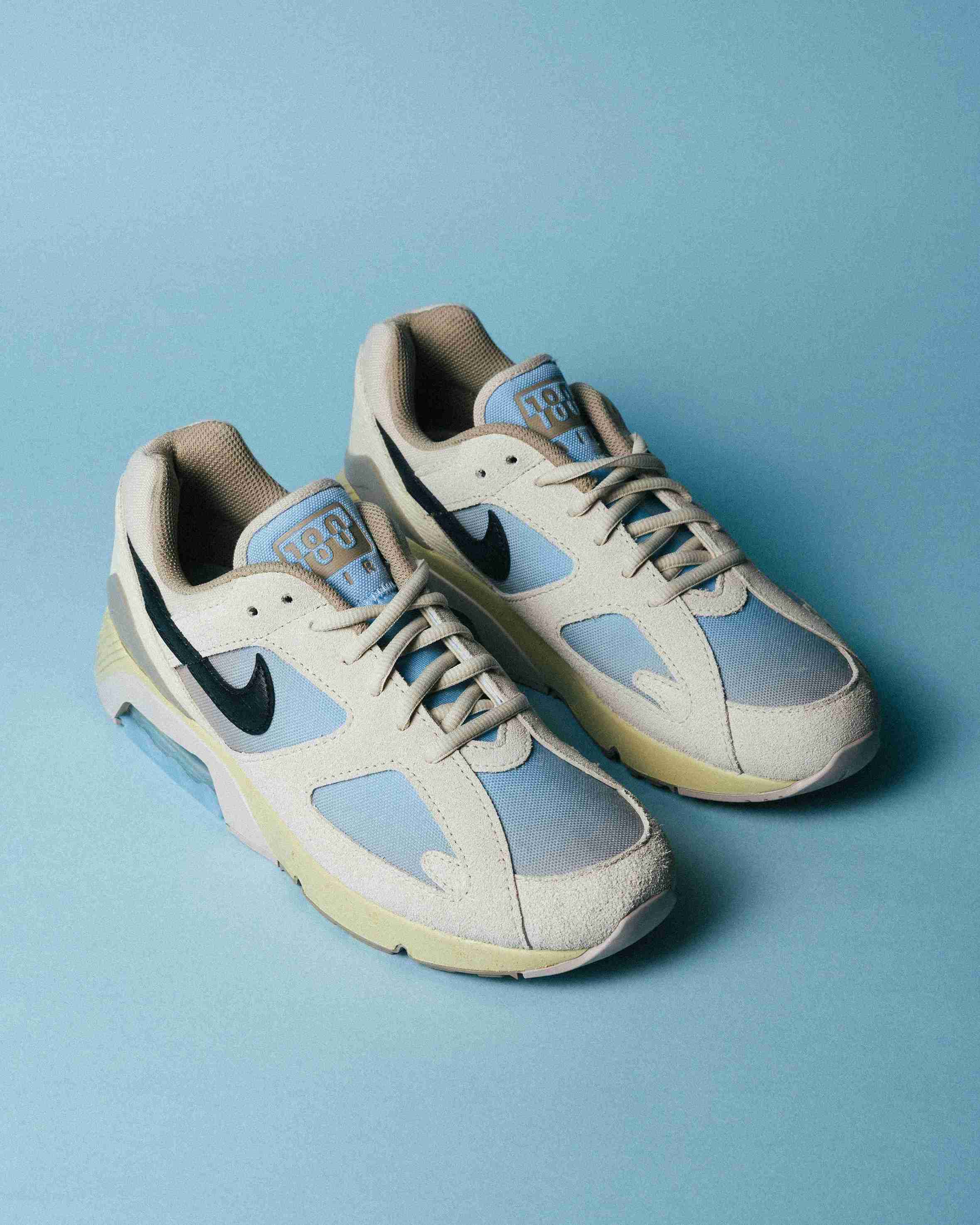 Paire de sneakers beige et bleu clair posée sur un fond bleu, vue de trois quarts avec mise en avant des formes et détails du modèle.